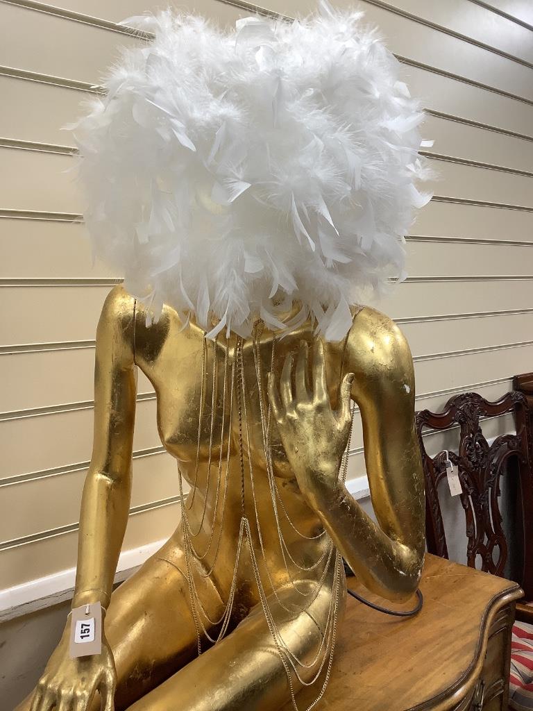 A large gilded seated female mannequin with illuminating feather shade, height 130cm